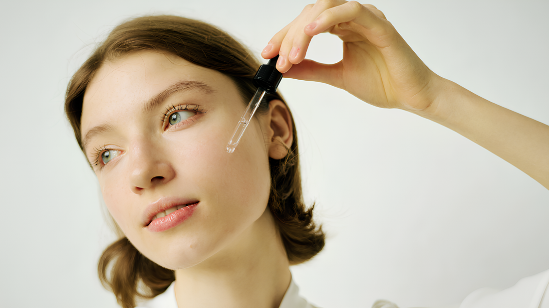 Model demonstrating face oil application for a glowing skincare routine, holding a dropper near her cheek.