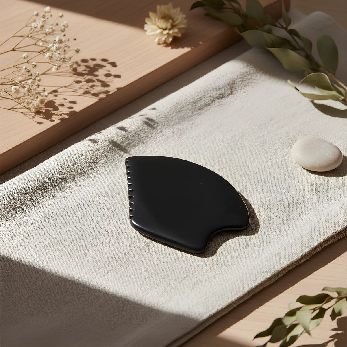 Gua Sha à cinq rebords en pierre naturelle posé sur une surface claire, symbole de beauté naturelle et de rituel bien-être.